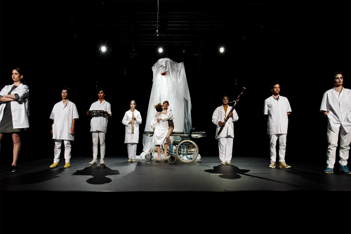 Le choeur des âmes en blanc, sur la scène du théâtre.
                      Au centre Laura, interprétée par Camille Varenne, lève de son lit d'hôpital Ogusto interprétée par Clémence Zakiri.